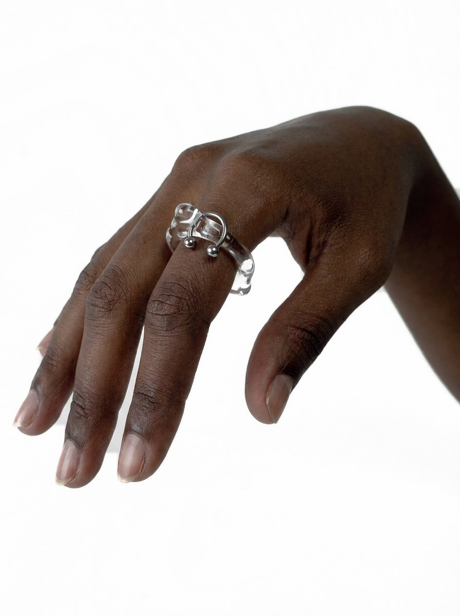 Pierced Glass Ring 0001 in clear hand-sculpted borosilicate glass with a stainless steel horseshoe piercing, worn on the hand, Rain and Rivers