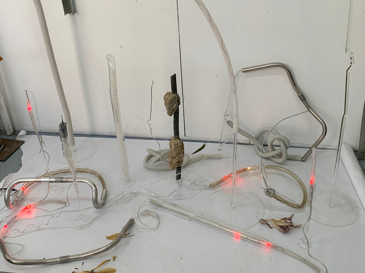 Installation of blown glass tubes and residual elements under red light on the studio floor