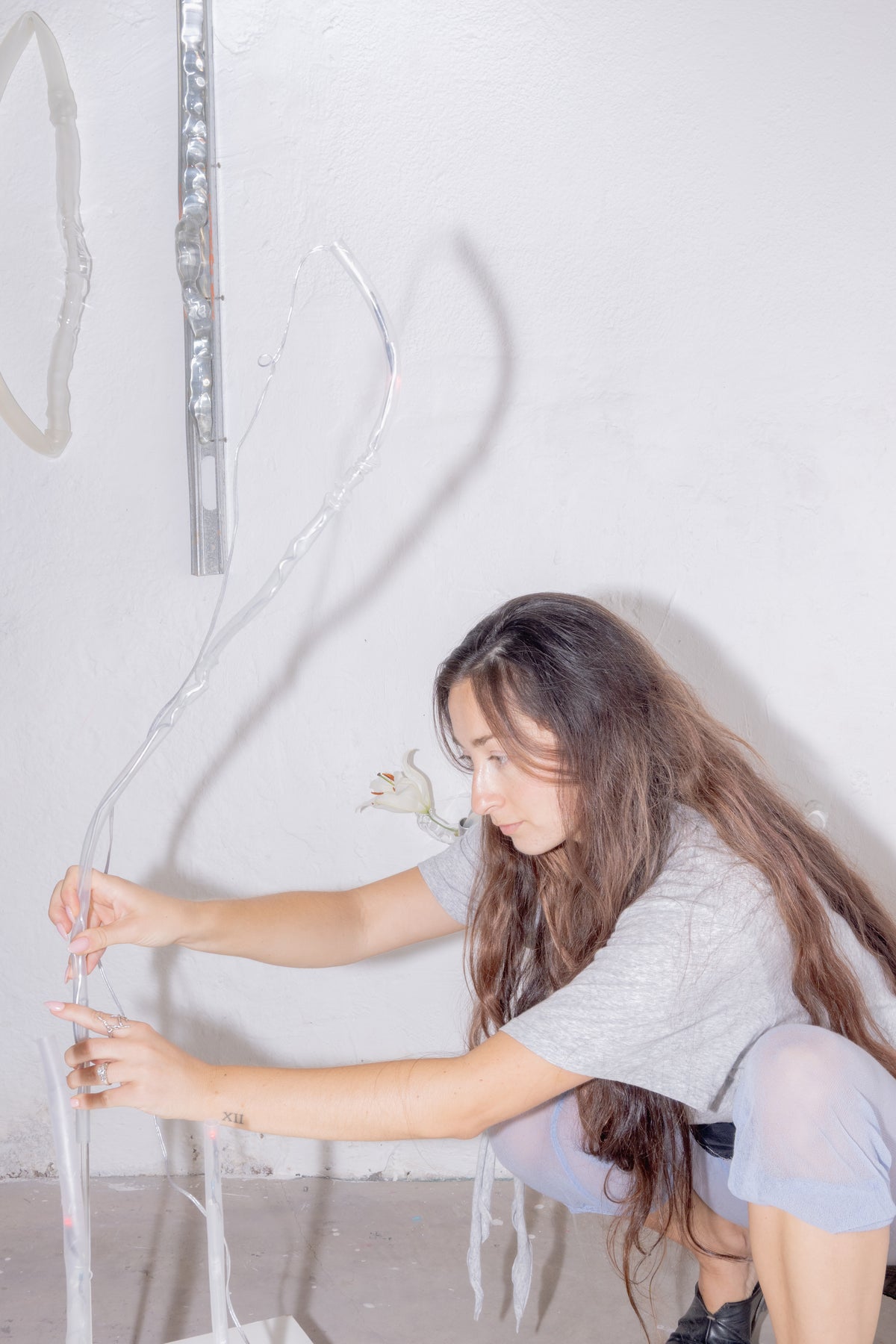 Magdalena Hart crouching beside hanging blown glass tubes in her studio